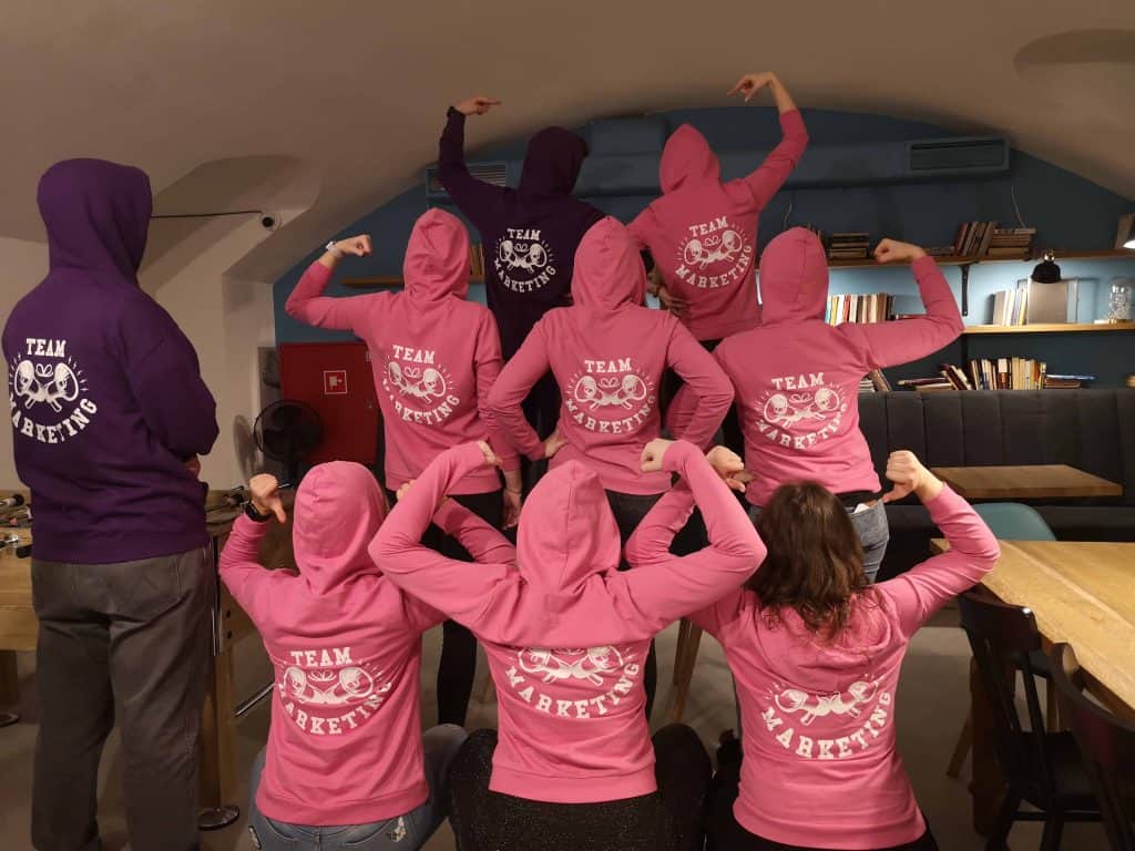 Grupa osób w różowych i fioletowyc bluzach z napisem Team Marketing
