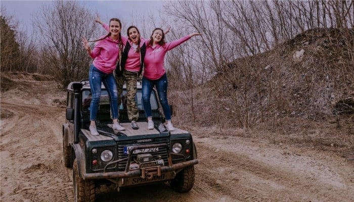Trzy młode dziewczyn stoją na masce samochodu terenowego 